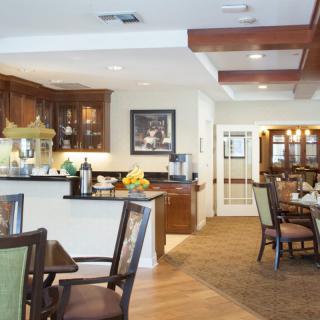 A cozy dining area with wooden floors, a kitchen counter, and several tables and chairs.