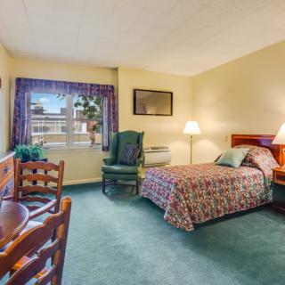 A cozy hotel room featuring a bed, chair, table, and a window with curtains.