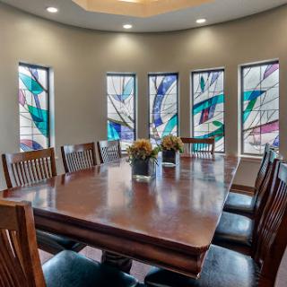 A stylish dining room featuring a large wooden table surrounded by chairs, illuminated by beautiful stained glass windows.