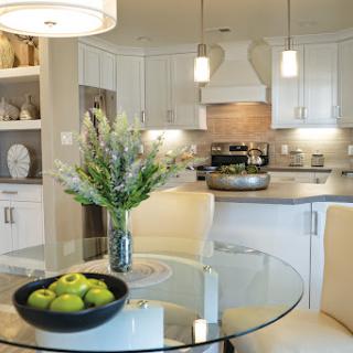A beautifully designed modern kitchen and dining area with a glass table, fresh flowers, and a bowl of green apples.