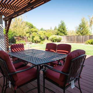A backyard patio with a table and chairs under a pergola, overlooking a garden.