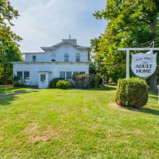 A quaint house with a sign on a lush green lawn surrounded by trees.