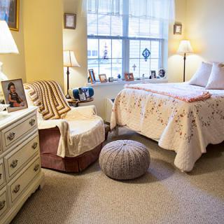 A cozy bedroom with soft lighting, featuring a bed, armchair, and decorative elements.