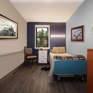 A cozy bedroom with a single bed, chair, and window, complemented by framed artwork and warm decor.