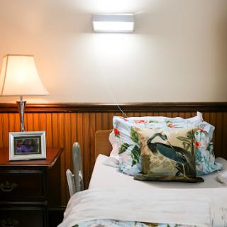 A cozy bedroom corner featuring a neatly made bed with decorative pillows, a bedside lamp, and a framed photo on the nightstand.