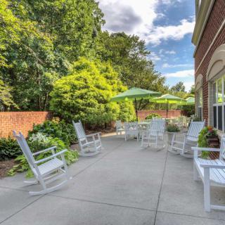 A sunny outdoor patio with rocking chairs and umbrellas, surrounded by lush greenery.