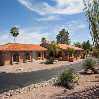 A single-story house with a desert landscape and palm trees.