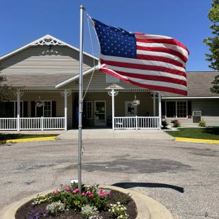 An American flag waves proudly in front of a building with a flower bed and inviting entrance.