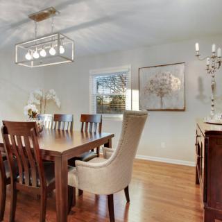 A modern dining room with a wooden table and chairs, featuring elegant lighting and wall art.