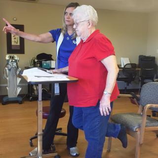 An elderly woman receives guidance from a physical therapist during a balance training session.