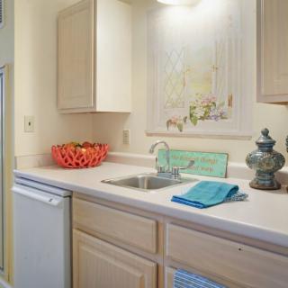A small kitchen area featuring light-colored cabinets, a countertop with a sink, and decorative items.
