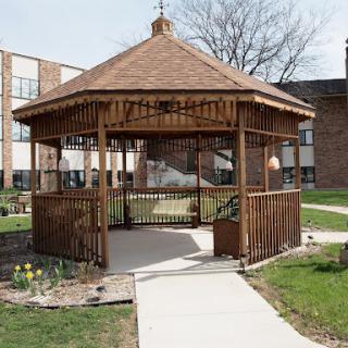 A serene wooden gazebo surrounded by green grass and flowers, inviting relaxation on a sunny day.
