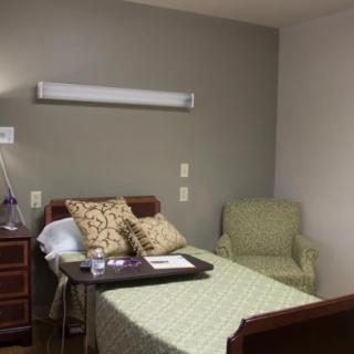 A hospital room featuring a bed with a tray, a chair, and bedside furniture.