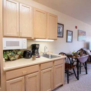 A cozy kitchenette area with wooden cabinets, a countertop featuring a microwave and coffee maker, and an adjacent dining table with chairs.