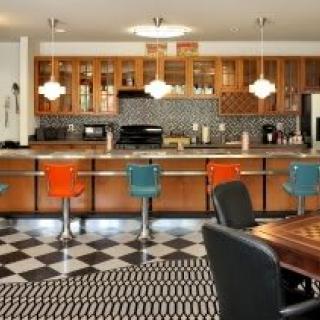 A retro-style kitchen with colorful bar stools, checkered flooring, and wooden cabinetry.