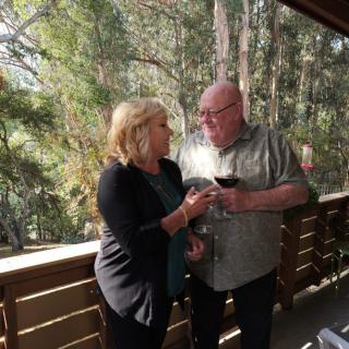 A couple enjoying a conversation on a balcony with wine and nature in the background.
