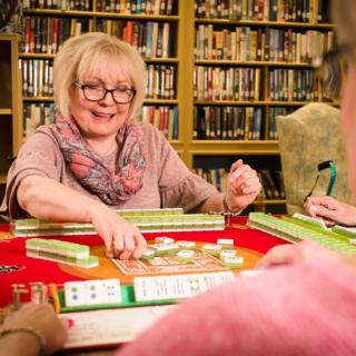 A group of people playing mahjong in a library setting.