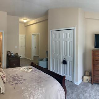 A cozy bedroom featuring a large bed, multiple dressers, a closet, and a mounted TV.
