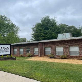 A brick building with a sign in front, set against a cloudy sky and grassy area.