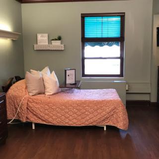 A cozy hospital room featuring a single bed with an orange quilt and a window offering natural light.