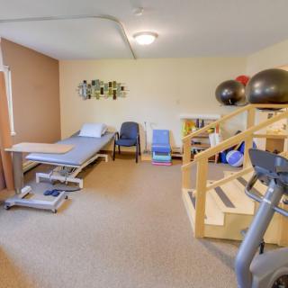 A rehabilitation room equipped with a treatment table, exercise equipment, and exercise balls.