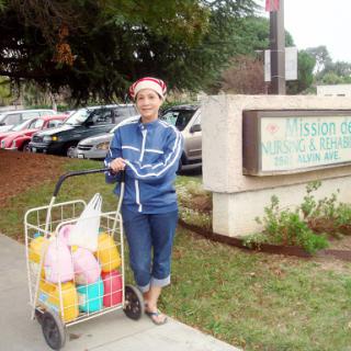 A woman standing next to a grocery cart filled with colorful bags in an urban setting.