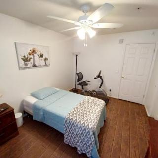 A cozy, minimalist bedroom featuring a bed with light blue bedding, an exercise bike, and decorative wall art.