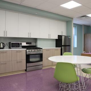 A modern office kitchen featuring appliances and a round dining table with green chairs.