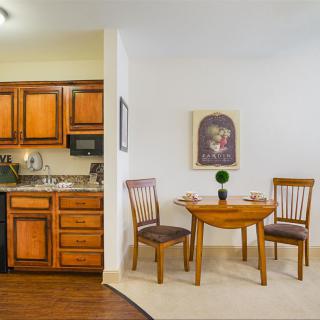 A cozy dining area with a small wooden table and chairs adjacent to an open kitchen featuring wooden cabinets.