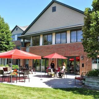 A sunny patio area with red umbrellas and people enjoying the outdoor seating in front of a brick building.