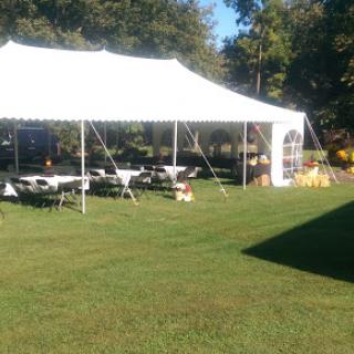 A spacious outdoor tent set up with tables on a grassy area, perfect for an event or gathering.