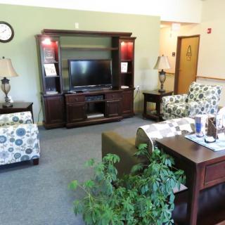A cozy living room with a television, sofas, armchairs, and decorative plants.