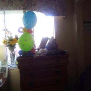 A cozy room featuring colorful balloons and a bouquet of flowers on a dresser by the window.