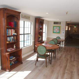 A cozy library area with bookshelves, tables, and chairs next to large windows.