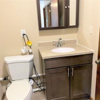 A small bathroom featuring a toilet, sink with a cabinet, and a mirror above.