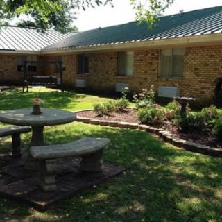 A peaceful garden setting with a stone bench and table in front of a brick house.
