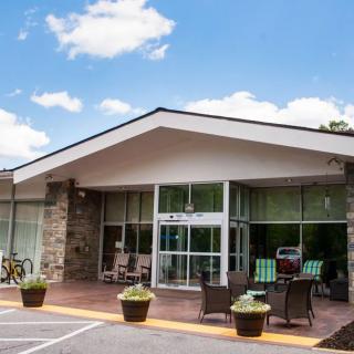 A modern building entrance with glass doors and patio furniture surrounded by plants.