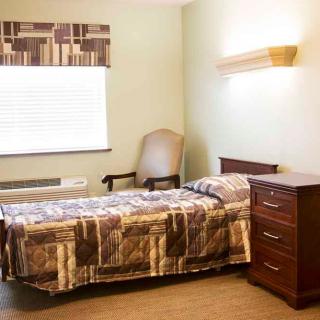 A simple bedroom with a single bed, a chair, and a dresser beside the window.