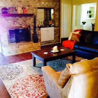 A cozy living room with a brick fireplace, comfortable seating, and a colorful decorative rug.