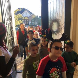 Children entering a festive holiday party dressed in Christmas-themed outfits.