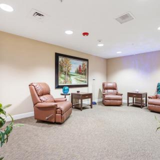 A cozy interior room featuring comfortable chairs, side tables, and a landscape painting on the wall.