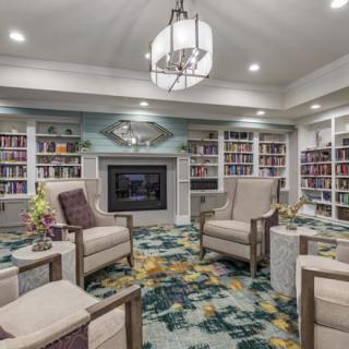 A cozy library room with comfortable armchairs, a fireplace, and bookshelves filled with books.