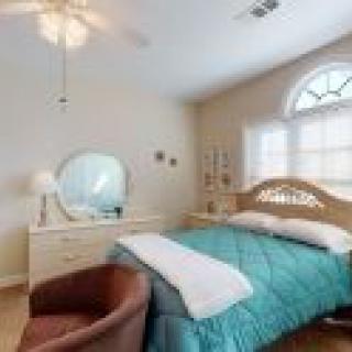 A cozy bedroom with a bed, dresser, and chair under natural light.