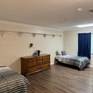 A spacious bedroom featuring two beds, a wooden dresser, and a blue curtain.
