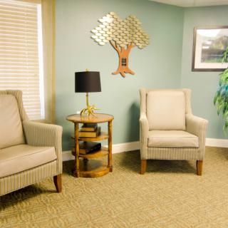 A cozy living room with comfortable chairs, a side table with a lamp, wall decor, and an indoor plant.