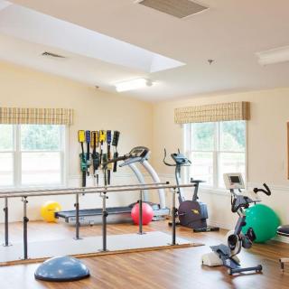 A well-lit gym room featuring various exercise equipment, including a treadmill, stationary bike, and therapy balls.