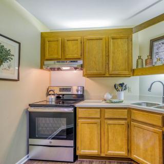A compact kitchen with wooden cabinets, a modern stove, and a corner sink.