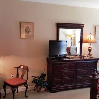 A cozy bedroom features a wooden dresser with a mirror, a small television, and a classic chair.
