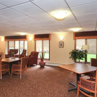 A cozy lounge area with tables, chairs, and ample natural light from large windows.