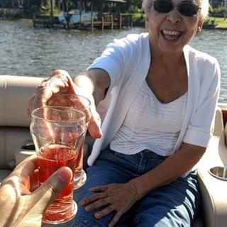 A joyful woman on a boat shares a toast with a friend by the lake.